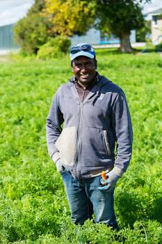 male migrant worker stands in farm field posing for camera