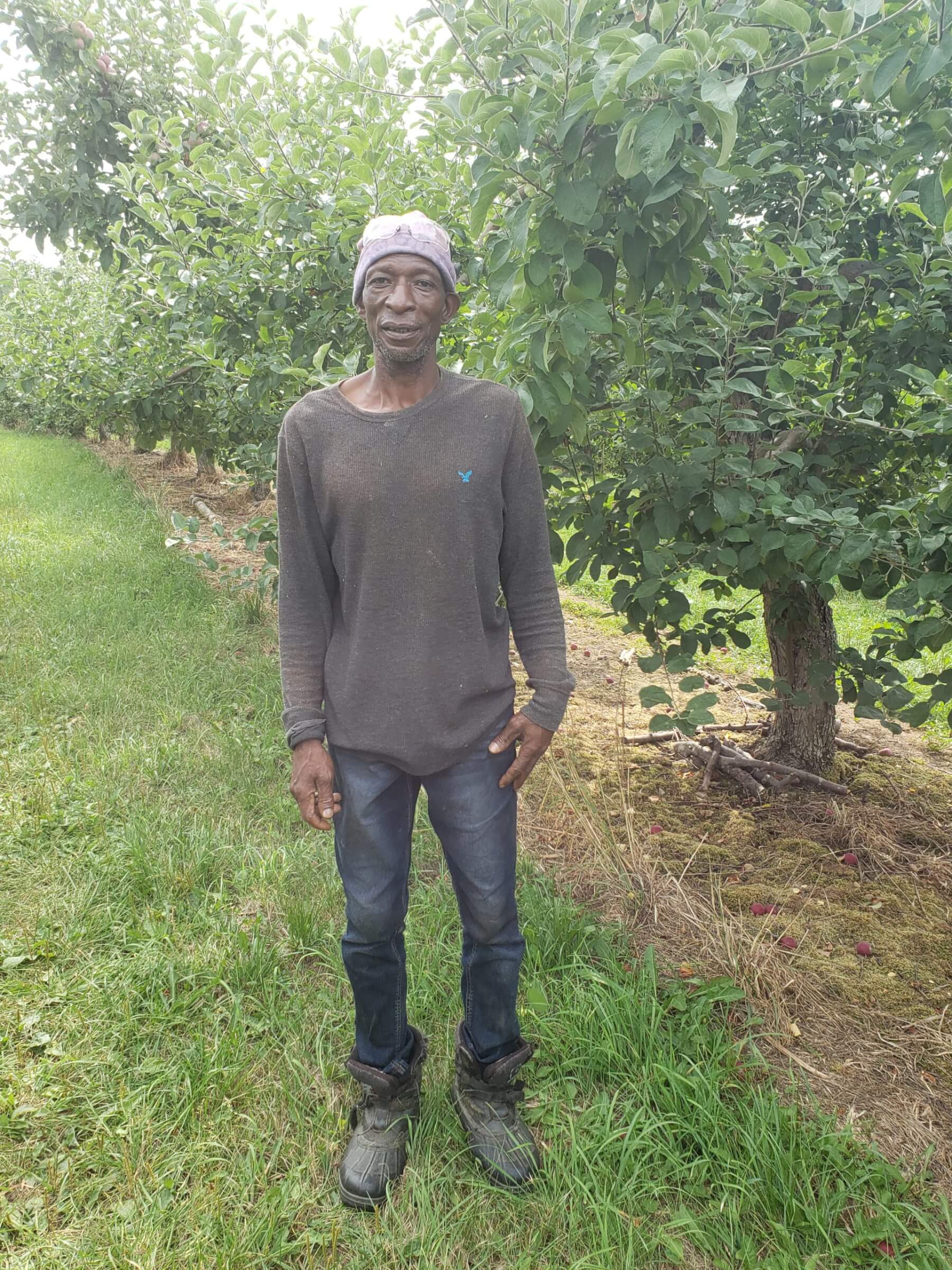 male migrant worker poses for camera in front of apple tree