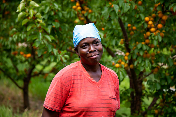 migrant worker smiles for camera, while standing in front of peach tree