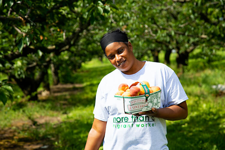 migrant worker holding basket of fruit smiling for the camera