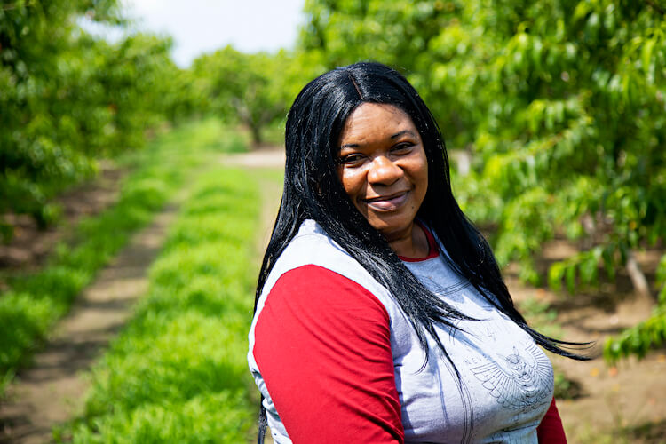 migrant worker smiles for camera in front of orchard