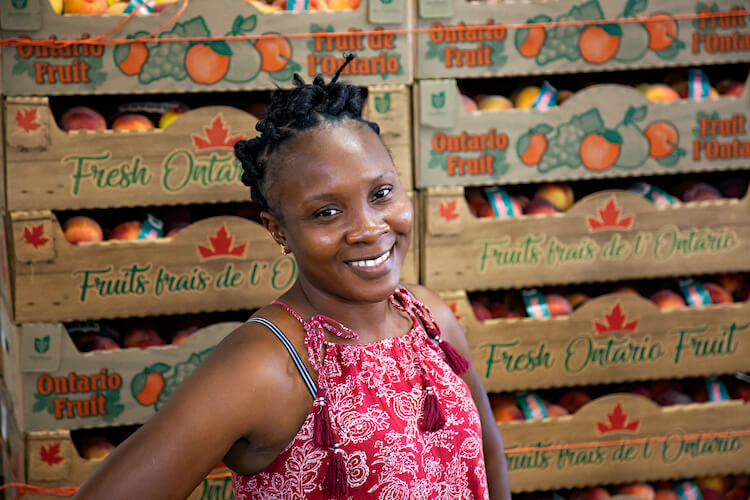 migrant worker smiling for camera in front of fruit boxes