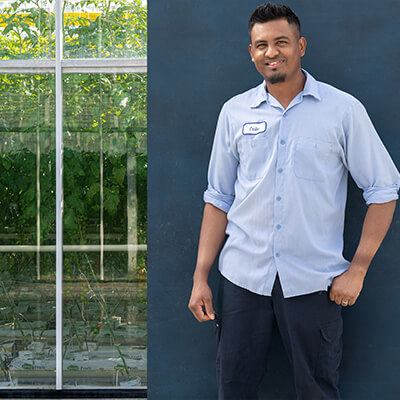 migrant worker posing for camera, while standing in front of farm