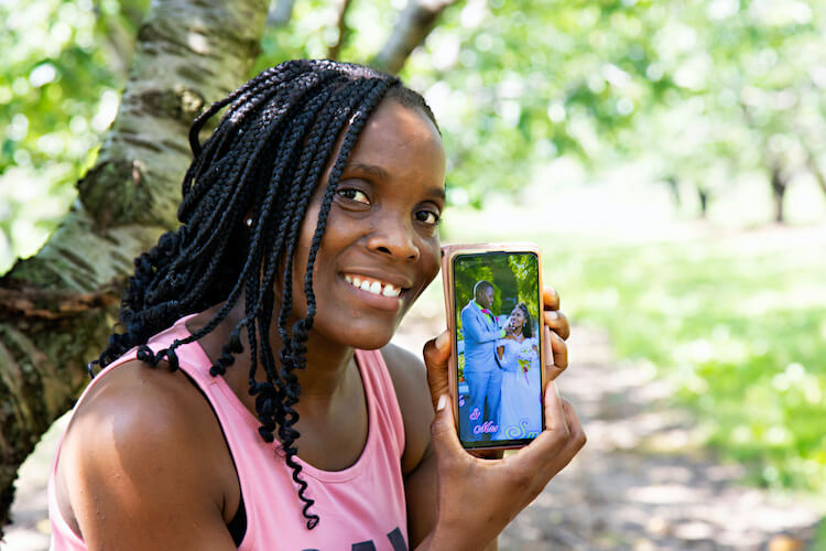 female migrant worker holds her phone while smiling for camera