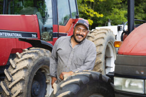 "Working here means more comforts for my family,” says Mexican migrant worker Carlos Rodriguez-Aburto Migrant farm worker in front of a tractor