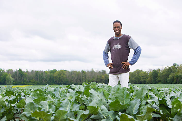 migrant worker standing in farm field smiling for the camera