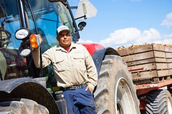male migrant worker stands in front of tractor