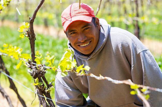 male migrant worker kneeling in farm field while smiling for camera